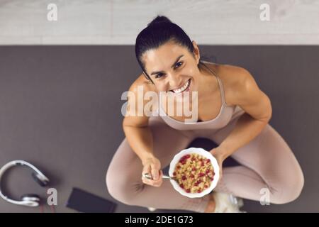 Glücklich fit Frau sitzt auf einer Sportmatte und genießen Gesunde Beeren Haferflocken Müsli Stockfoto
