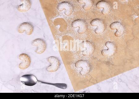 Halbmondförmige weihnachtsplätzchen "Vanillekipferl" genannt, ein traditionelles österreichisches oder deutsches Weihnachtsplätzchen mit Nüssen und Puderzucker auf Backpapier Stockfoto