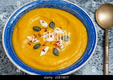 Geröstete Kürbis- und Karottensuppe mit Sahne und Kürbiskernen im Hintergrund. Nahaufnahme Stockfoto