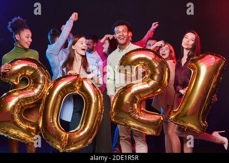 Die Feier Zum Neuen Jahr. Gruppe von jungen glücklichen multiethnischen Menschen mit goldenen Folienballons in Form von Zahlen 2021 und Spaß an der Weihnachtsfeier. Urlaubskonzept Stockfoto