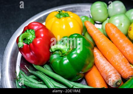 Selektive Konzentration von grünem Paprika, grünen Bohnen, rotem Paprika, Karotten auf einem Edelstahlteller mit verschiedenen Gemüsesorten Stockfoto