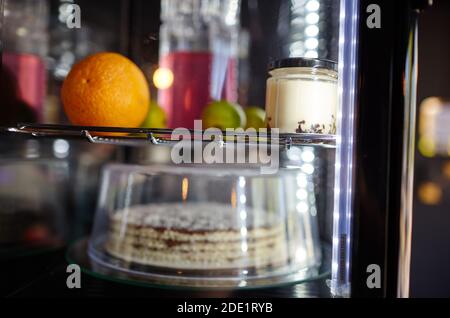 Verschwommenes Bild von Showcase im Café-Shop. Kuchen und Krug mit Getränk auf den Regalen eines Fensters eines Straßenrestaurants Stockfoto