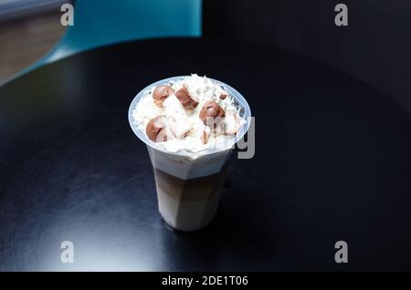 Einweg-Plastikbecher mit leckeren Kaffee Getränk mit Milch, Schlagsahne, Eis und Schokolade Bar mit Kokosnuss Kopfgeld auf Holztisch im Café Stockfoto