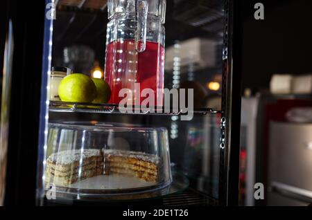 Verschwommenes Bild von Showcase im Café-Shop. Kuchen und Krug mit Getränk auf den Regalen eines Fensters eines Straßenrestaurants Stockfoto