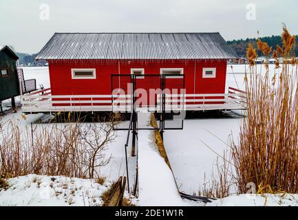 Rote Holzhütte auf dem gefrorenen See. Winterzeit am Angelsee. Stockfoto