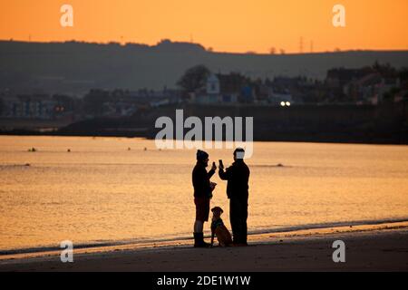 Portobello, Edinburgh, Schottland, Großbritannien. 28. November 2020. Kühler Sonnenaufgang Temperatur 3 Grad am Meer von Portobello.Bild: Zwei Hundespaziergänger mit ihrem Hund am Ufer des Firth of Forth. Quelle: Arch White/Alamy Live News. Stockfoto