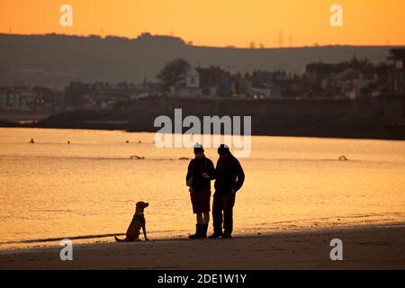 Portobello, Edinburgh, Schottland, Großbritannien. 28. November 2020. Kühler Sonnenaufgang Temperatur 3 Grad am Meer von Portobello.Bild: Zwei Hundespaziergänger mit ihrem Hund am Ufer des Firth of Forth. Quelle: Arch White/Alamy Live News. Stockfoto