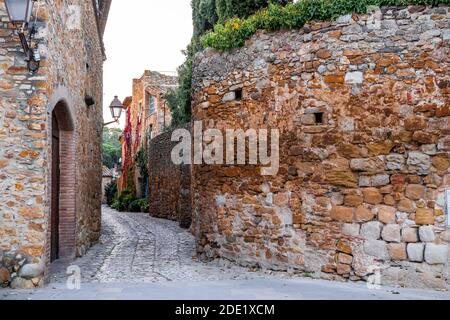 Enge mittelalterliche gepflasterte Gasse mit einer Mauer aus Stein bedeckt Von Pflanzen in Peratallada Stockfoto