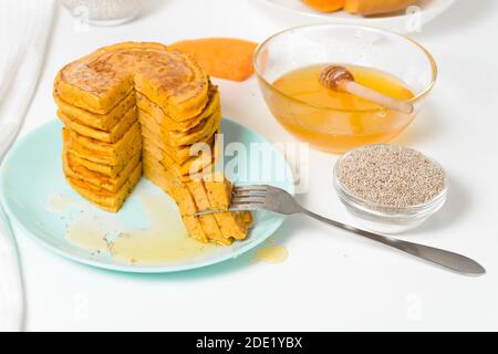 Ein Stapel von Herbst Kürbis Pfannkuchen mit Chia Samen und Honig auf einem hellen Hintergrund. Köstliche gesunde vegetarische Ernährung Frühstück. Das Konzept der Einnahme Stockfoto