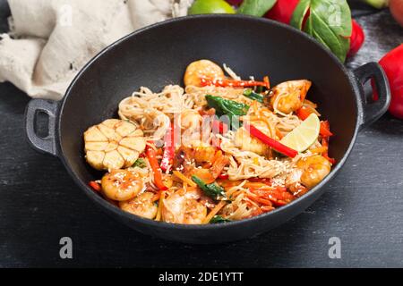 Gebratene Nudeln mit Garnelen und Gemüse im Wok umrühren Auf dunklem Hintergrund Stockfoto
