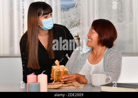 Eine glückliche asiatische Frau hält eine goldene Geschenkbox und sieht eine junge Frau mit einer Gesichtsmaske an. Secret Santa Konzept. Stockfoto