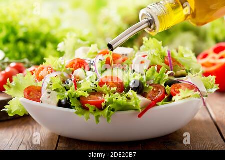 Kochen Salat. Olivenöl Gießen in Schüssel mit frischem Gemüsesalat Stockfoto