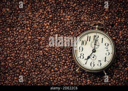 Nahaufnahme eines alten Weckers auf dem Hintergrund mit vielen gerösteten Kaffeebohnen und Kopierraum, Vollformat. Stockfoto