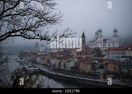 Passau, Deutschland. November 2020. Eine Krähe sitzt auf einem Zweig vor der Skyline von Passau, die von Nebel bedeckt ist. Angesichts der stark gestiegenen Zahl von Coronainfektionen sind in Passau seit Samstag strenge Ausreisebeschränkungen in Kraft.Quelle: Lino Mirgeler/dpa/Alamy Live News Stockfoto