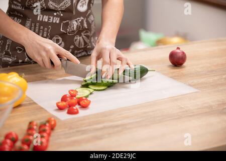 Frauenhände schneiden Gurke, hinter frischem Gemüse in der Küche Stockfoto