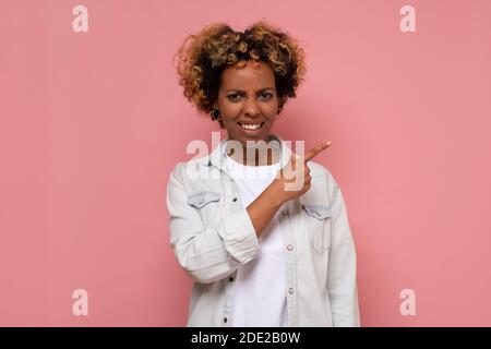 Afroamerikanische Frau mit trauriger Grimasse, zeigt Daumen beiseite, drückt Reue Emotionen. Studio auf rosa Wand aufgenommen. Stockfoto
