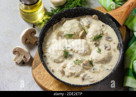 Hausgemachte Fleischbällchen in saurer Sahne-Sauce mit Pilzen in einer Pfanne auf Stein- oder Schiefertisch. Stockfoto
