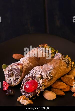 Zwei Cannoli auf einem schwarzen Teller, EIN traditionelles italienisches Dessert aus Frischkäse und Pistazien. Stockfoto