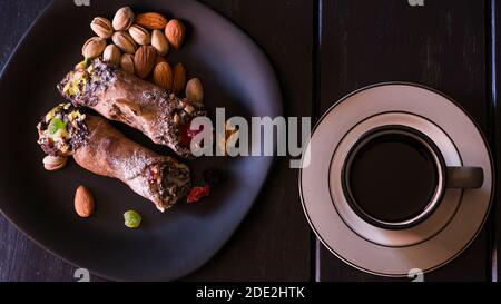 Zwei Cannoli auf einem schwarzen Teller, EIN traditionelles italienisches Dessert aus Frischkäse und Pistazien mit Kaffee. Stockfoto