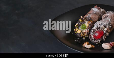 Zwei Cannoli auf einem schwarzen Teller, EIN traditionelles italienisches Dessert aus Frischkäse und Pistazien. Stockfoto