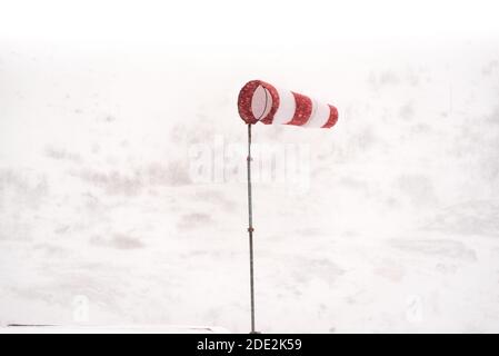 Windsack in einem Schneesturm flattert im Wind isoliert Vor dem weißen Hintergrund schneebedeckter Berge Stockfoto