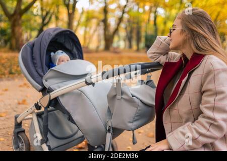 Mama sitzt auf der Bank im Park und schaut auf die Baby, das im Kinderwagen ist Stockfoto