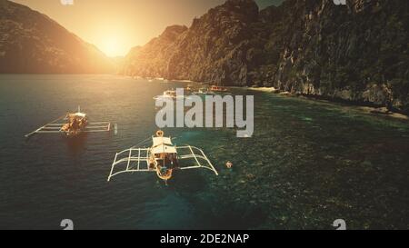 Sonnenuntergang in Nahaufnahme Passagierboote an Kliff Ozean Küste Luftbild. Touristen schwimmen, tauchen im dunklen Meer Bucht Wasser an der Felsküste der Palawan Insel, Philippinen, Asien. Filmische Sonne untergeht Seestück Drohne erschossen Stockfoto