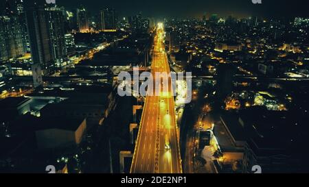 Nachts beleuchtete Stadtlandschaft mit Verkehrsautobahn im Business Center Aerial. Epische Dämmerung Stadt in Neonlicht an von Laternen Straße mit Autos beleuchtet, LKW fahren. Philippinen Hauptstadt Manila Straßen Stockfoto