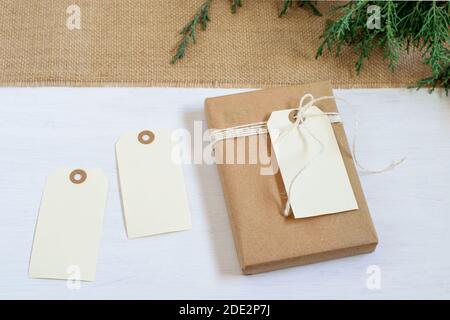 Handgemachtes Geschenk in braunem Bastelpapier gewickelt, Knoten auf dem Quappen texturierten Textil gebunden. Weiße leere Karten, Thuja-Baumzweige. Schönes umweltfreundliches Geschenk f Stockfoto