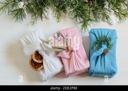 Festliche Geschenke verpackt in verschiedenen Textilbekleidung im furoshiki-Stil auf dem weihnachtlichen Hintergrund. Schöne Alternative handgemachte Geschenke. Keine Verschwendung, Wiederverwendung Stockfoto