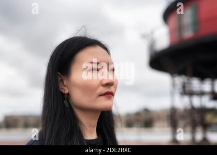 Eine chinesische Frau tief in Gedanken in der Nähe der sieben Fuß Knoll Leuchtturm verschwommen im Hintergrund mit einem grau bewölkten Tag in Baltimore Maryland. Stockfoto