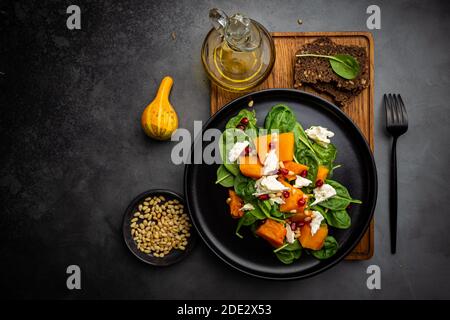 Salat mit geröstetem Kürbis, Käse, Spinat, Pinienkernen und Gewürzen auf dunklem Hintergrund, Draufsicht Stockfoto