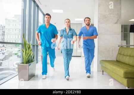 Drei Doktoren, die durch den Krankenhauskorridor laufen, der in einem ist Beeil dich Stockfoto