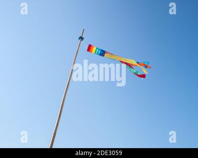 Regenbogenfarbene Windsocke flattert im Wind auf einem Blauer Himmel Tag Stockfoto