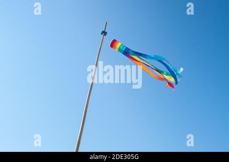 Regenbogenfarbene Windsocke flattert im Wind auf einem Blauer Himmel Tag Stockfoto