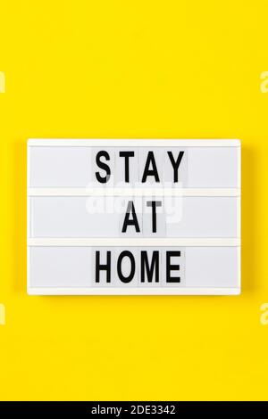 Leuchtkasten mit Text ZU HAUSE bleiben auf gelbem Hintergrund. Gesundheitswesen, Medizin, Quarantänekonzept Stockfoto