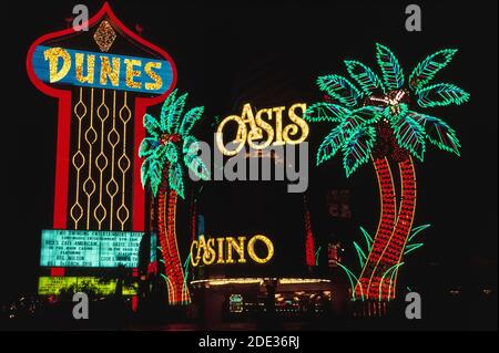 Neon und andere bunte Lichter machten diese Outdoor-Schilder für das Dunes Hotel und sein Oasis Casino in der Nacht am Las Vegas Boulevard, besser bekannt als der Strip, eine Straße gesäumt mit spektakulären Resort-Hotels und Casinos südlich der Stadtgrenze von Las Vegas, Nevada, USA. Die Dünen wurden 1955 eröffnet, eine frühe Attraktion in dieser berüchtigten Wüstendestination, die für ihre Glücksspiele und guten Zeiten bekannt ist. Als das Hotel 1993 abgerissen wurde, um Platz für das neue Bellagio Mega-Resort zu schaffen, gingen diese Wahrzeichen und Neonpalmen der Geschichte verloren. Stockfoto