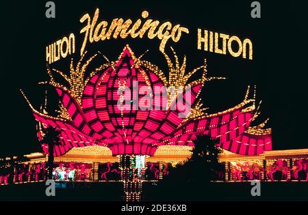 Neon und andere bunte Lichter machten dieses Outdoor-Schild für das Flamingo Hotel & Casino bei Nacht am Las Vegas Boulevard, besser bekannt als der Strip, eine Straße mit spektakulären Resort-Hotels und Casinos südlich der Stadtgrenze von Las Vegas, Nevada, USA. Das Flamingo wurde 1946 eröffnet, eine sehr frühe Attraktion in diesem berüchtigten Wüstenziel, das für sein Glücksspiel und seine guten Zeiten bekannt ist. Das Hotel gehörte der Hilton Corp., als dieses historische Foto im Jahr 1983 aufgenommen wurde. Ein Jahrzehnt später wurde das ursprüngliche Hotel abgerissen, aber dieses einzigartige Zeichen von stilisierten rosa Federn wurde gerettet. Stockfoto