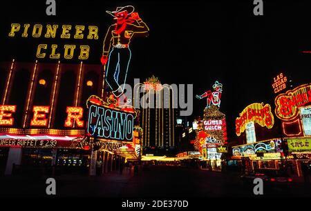 Neon und andere bunte Lichter machten diese Outdoor-Schilder für Casinos und Hotels in der Nacht und während des Tages an der Fremont Street, dem ursprünglichen Stadtzentrum für Glücksspiel und gute Zeiten in Las Vegas, Nevada, USA, hervorstechen. Leicht zu erkennen in der Neon-Anzeige sind ein Cowboy und ein Cowgirl mit dem Spitznamen Vegas Vic und Vegas Vickie. Seit der Aufnahme dieses historischen Fotos im Jahr 1983 wurde die Fremont Street mit einem Baldachin bedeckt, das die längste Videowand der Welt ist und Besuchern in der Fußgängerzone eine Sound-and-Light-Show über dem Kopf präsentiert. Stockfoto