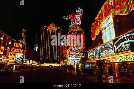 Neon und andere bunte Lichter machten diese Outdoor-Schilder für Casinos und Hotels in der Nacht und während des Tages an der Fremont Street, dem ursprünglichen Stadtzentrum für Glücksspiel und gute Zeiten in Las Vegas, Nevada, USA, hervorstechen. Leicht zu erkennen in der Neon-Display ist ein Cowgirl namens Vegas Vickie. Seit der Aufnahme dieses historischen Fotos im Jahr 1983 wurde die Fremont Street mit einem Baldachin bedeckt, das die längste Videowand der Welt ist und Besuchern in der Fußgängerzone eine Sound-and-Light-Show über dem Kopf präsentiert. Die leuchtenden Lichter der Neonschilder tauchten erstmals 1929 in Las Vegas auf. Stockfoto