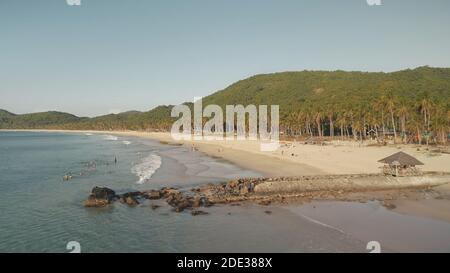 Familienurlaub auf Paradiesinsel mit Sandstrand. Luftwasserbucht mit Menschen ruhen am seichten Wasser. Palmen und sandige Ozeanküste der Insel El Nido, Philippinen. Drohnenaufnahme im Kino Stockfoto