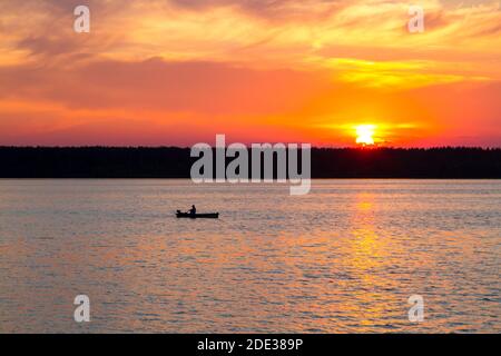 Sonnenuntergang auf dem See. Ein Fischer fischt von einem Boot aus Stockfoto