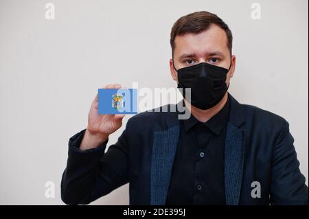 Spanisch Mann tragen schwarz formell und schützen Gesichtsmaske, halten Melilla Flagge Karte isoliert auf weißem Hintergrund. Spanien autonome Gemeinschaften Coronavirus Cov Stockfoto