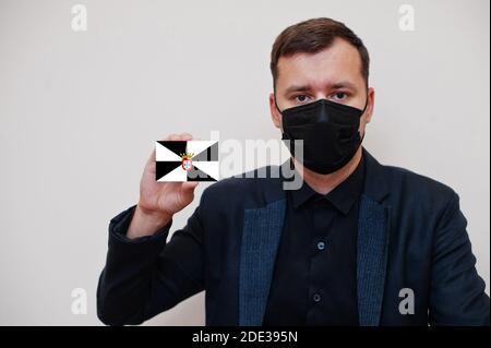 Spanisch Mann tragen schwarz formell und schützen Gesichtsmaske, halten Ceuta Flagge Karte isoliert auf weißem Hintergrund. Spanien autonome Gemeinschaften Coronavirus Covid Stockfoto