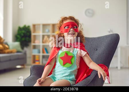Portrait von Lachen glücklich rothaarige Mädchen in Kostüm von Superhelden-Star sitzt auf dem Sessel und lächelt Stockfoto