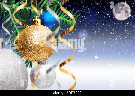 Weihnachtsdekoration. Goldene und silberne Kugeln, Streamer hängen auf Fichtenzweig auf blau verschneiten Hintergrund. Weihnachtskarte mit Kopierplatz Stockfoto