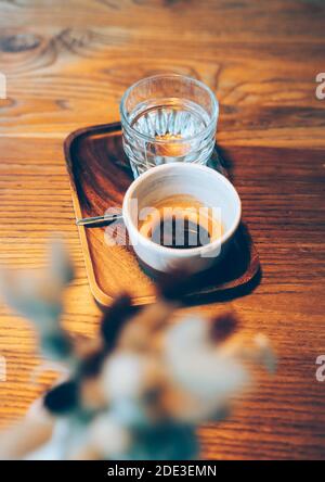 Tasse Espresso und ein Glas Wasser auf einem Holztisch in einem gemütlichen kleinen Café. Weitwinkelansicht Stockfoto