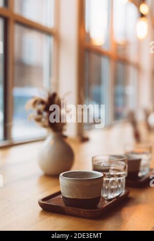 Tasse Kaffee Espresso und Glas Wasser auf Holz Tisch in der Nähe des Fensters in einem gemütlichen kleinen Café Stockfoto