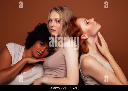 Junge hübsche kaukasische, afro, skandinavische Frau posiert fröhlich zusammen auf braunem Hintergrund, Lifestyle diverse Nationalität Menschen Konzept Stockfoto