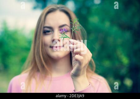 Junge kaukasische Dame in rosa Pullover hält kleine gezupft Blume auf ihren Händen während des Gehens Stockfoto